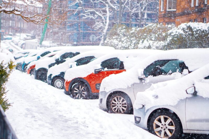 Snow-covered cars lined up on a wintry Hamilton street, highlighting the need for seasonal vehicle care.