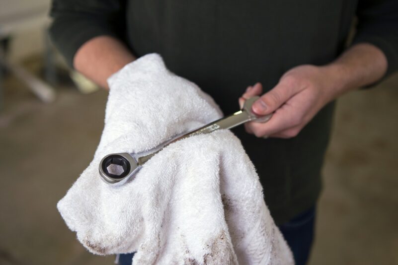 Car Services Essentials in Hamilton Mechanic holding a ratchet, wiping it clean with a white towel.