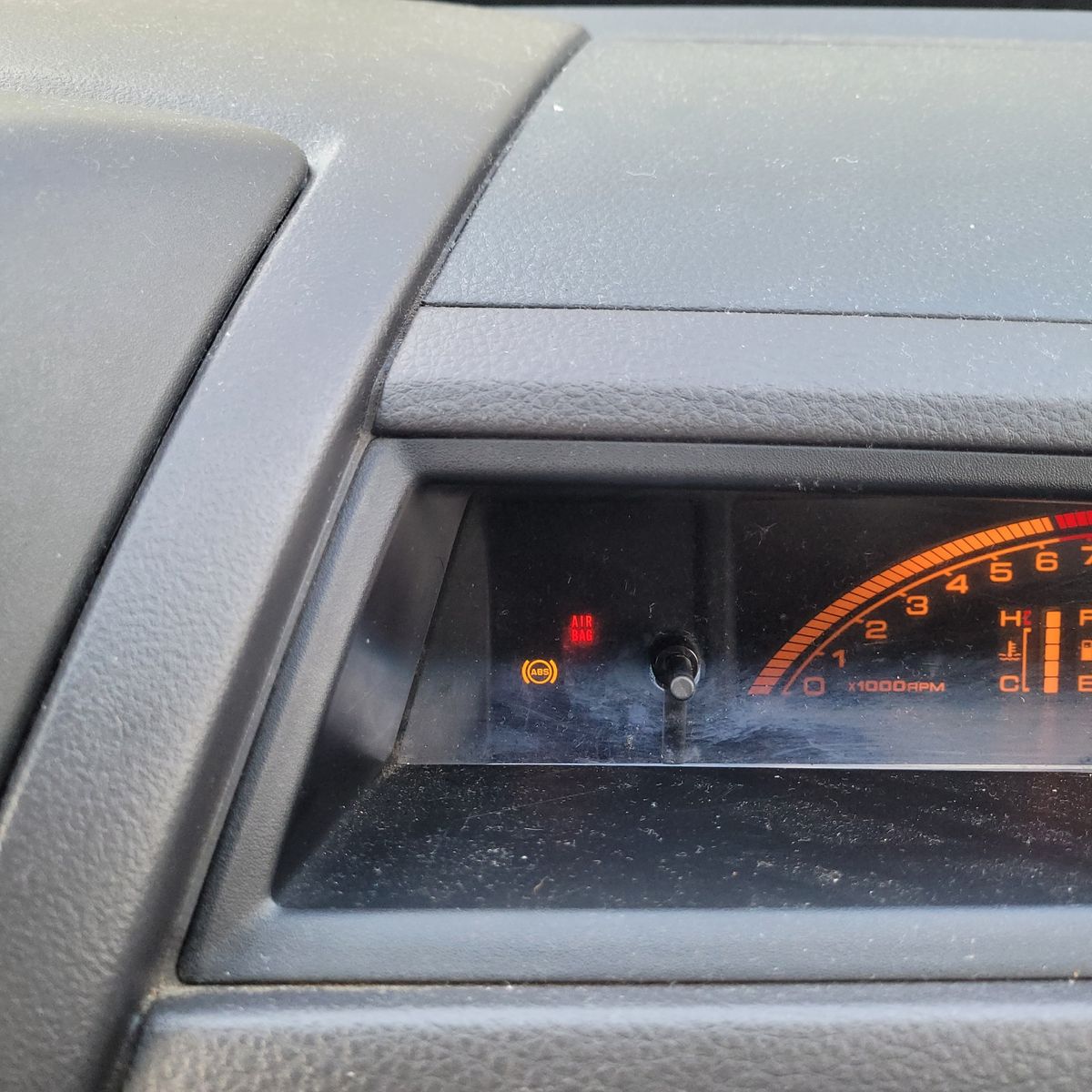 Close-up of car dashboard showing ABS and airbag warning lights illuminated.