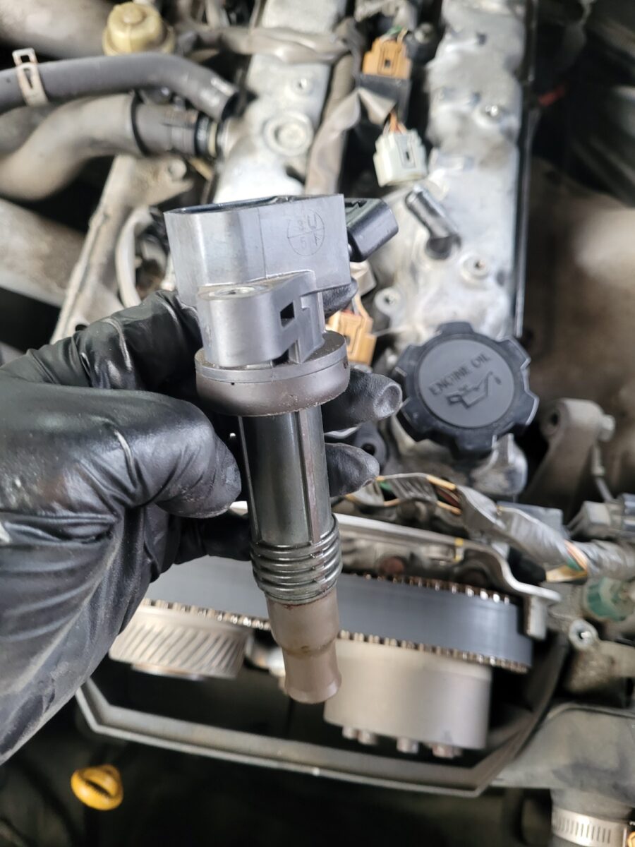 A gloved hand holds a car ignition coil over an engine. A gloved hand holds a car ignition coil over an engine.