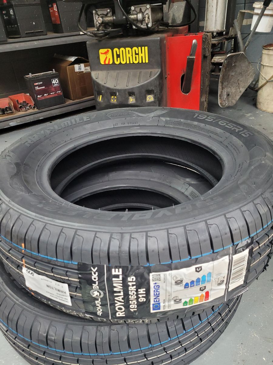 Stack of new Royalmile car tyres beside a tyre fitting machine in a workshop.