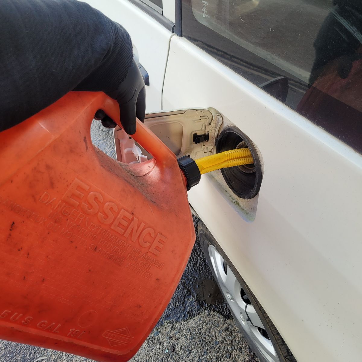 Hand pouring gasoline from red fuel container into white car’s gas tank