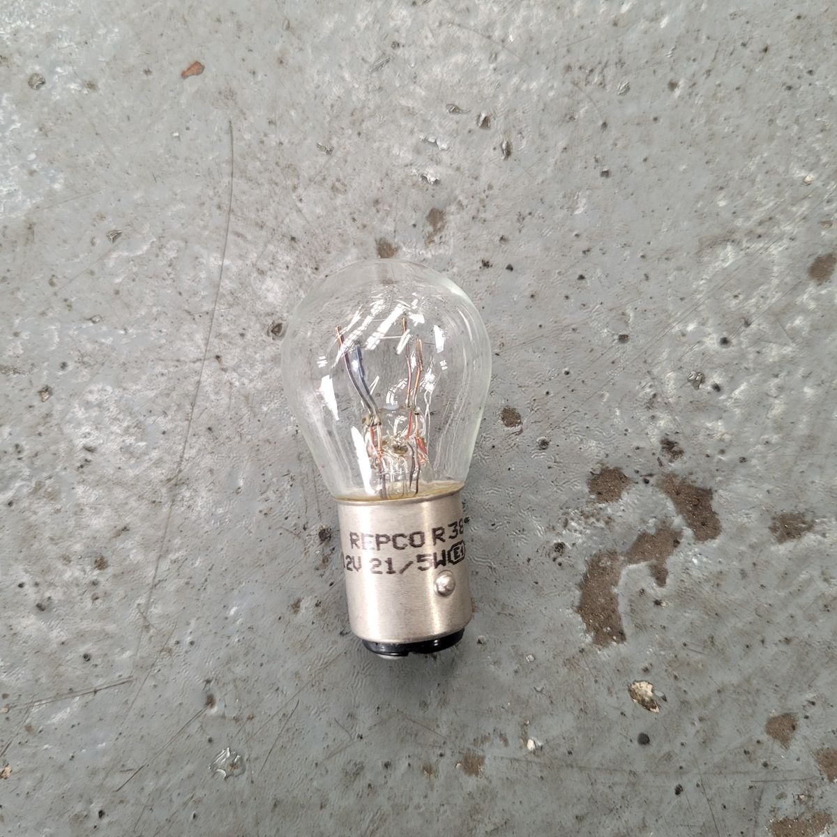 Clear Automotive Parking Light Bulb on Concrete Surface Single clear parking light bulb resting on a rough gray concrete floor.