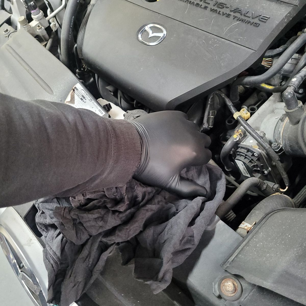 Gloved hand removing radiator cap on Mazda engine with cloth