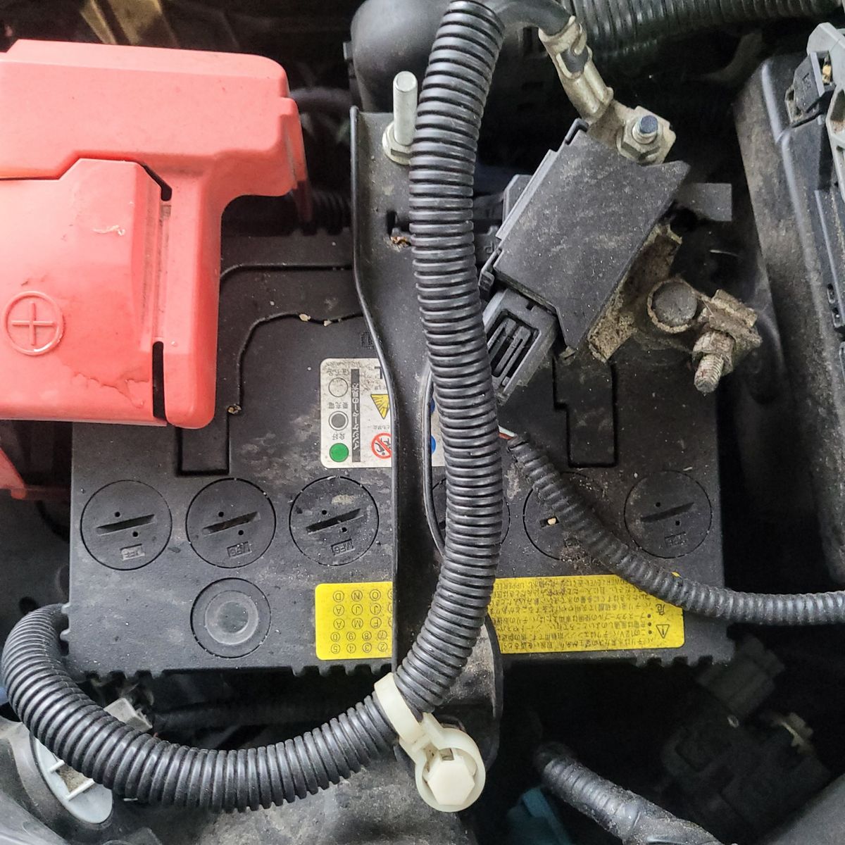 Top view of a 12V car battery installed in an engine bay Close-up of a 12V car battery with cables and terminals attached