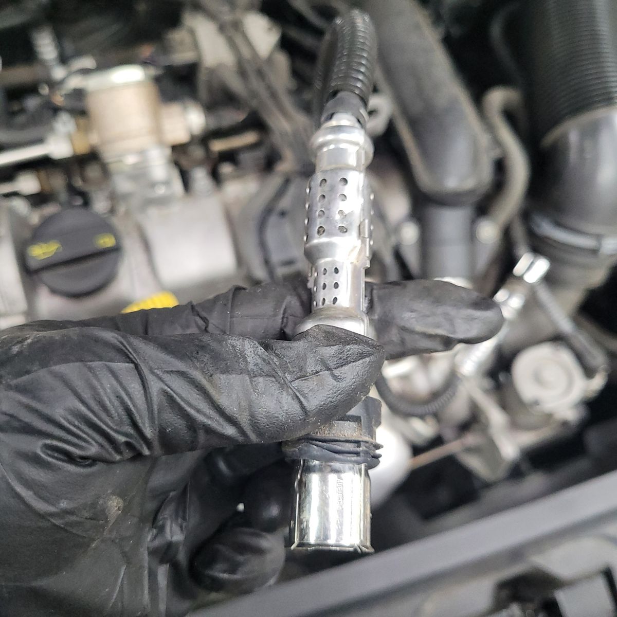 Mechanic holding oxygen sensor in car engine bay for diagnostic check