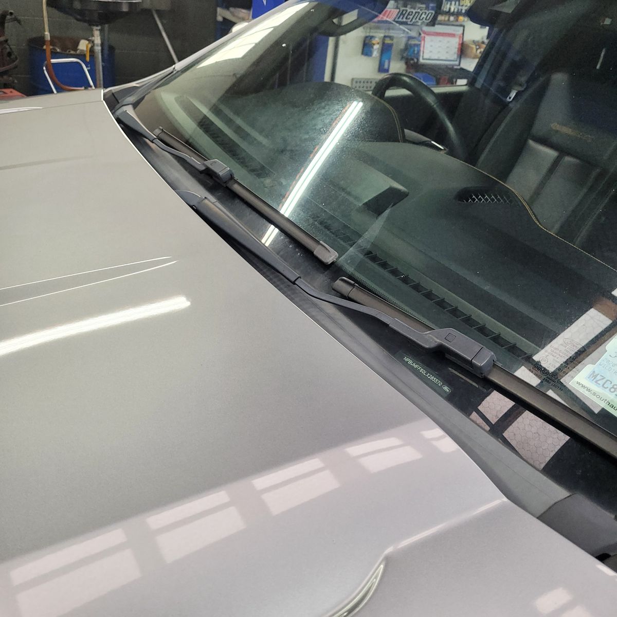 Pair of windshield wiper blades on a car windshield in a garage.
