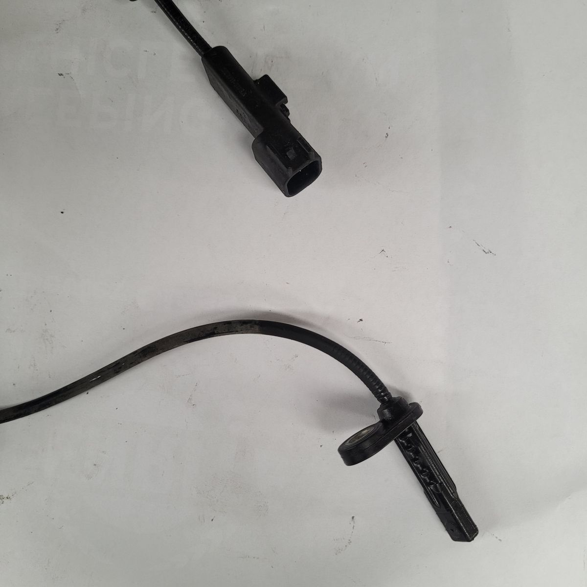 Automotive ABS Sensor on White Background A black automotive ABS sensor with connector and cable, lying on a white surface.