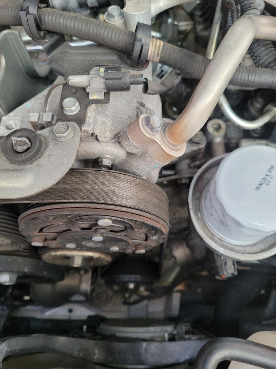 Vehicle air conditioning compressor with attached hoses and belt in engine compartment.