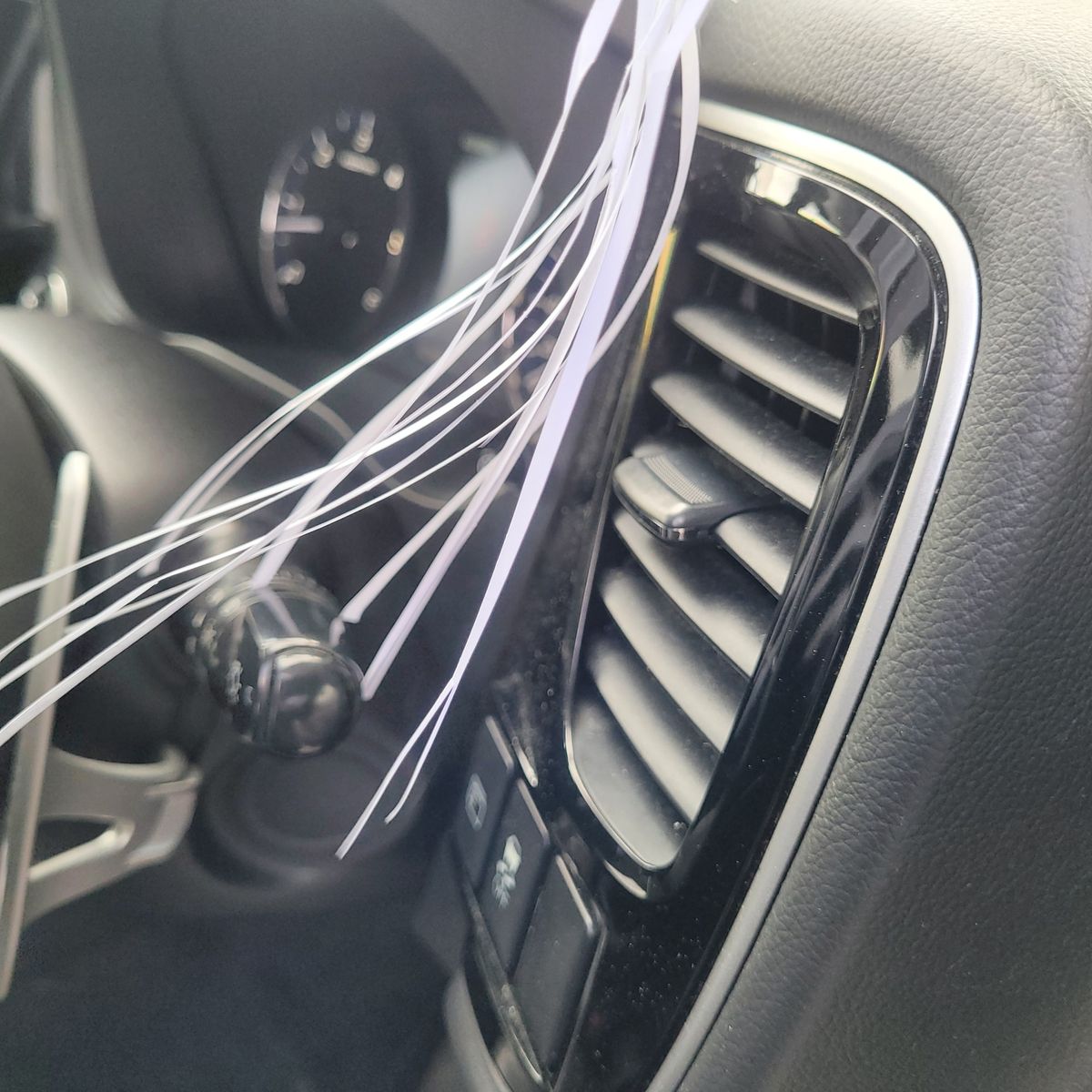 Car air vent with control buttons and decorative white ribbons nearby