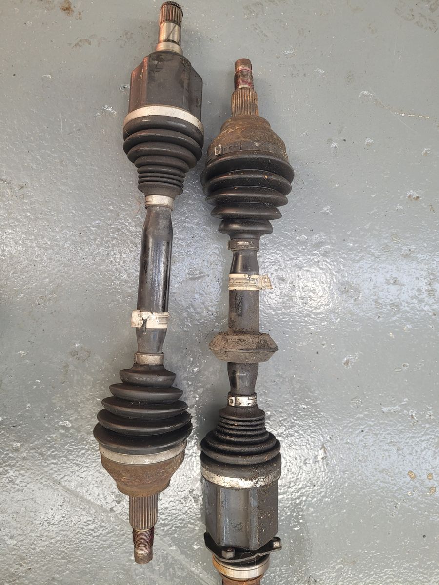 Old and New Car Axles Side by Side Two car axles, one cleaner and newer, one dirty and worn, on a workshop floor.