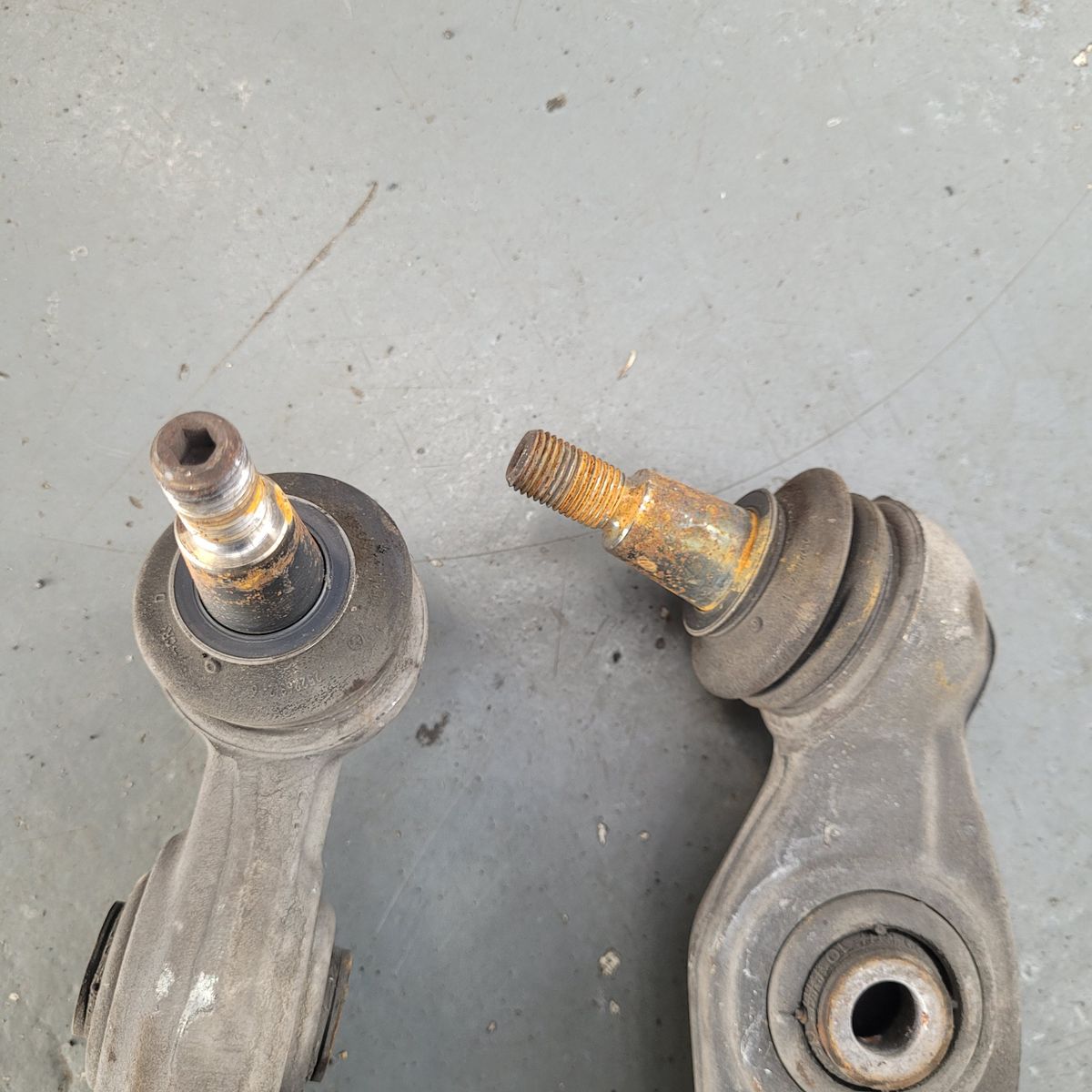 Two old, worn ball joints with rust and dirt on a gray shop floor