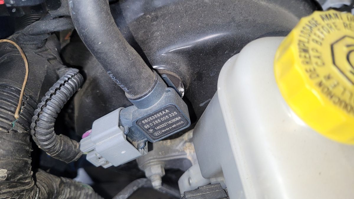 Close-up of a brake booster vacuum sensor connected to a vacuum line.