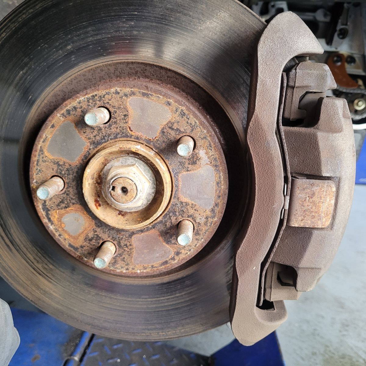 Rusty car brake caliper and rotor viewed from the side of the wheel hub.