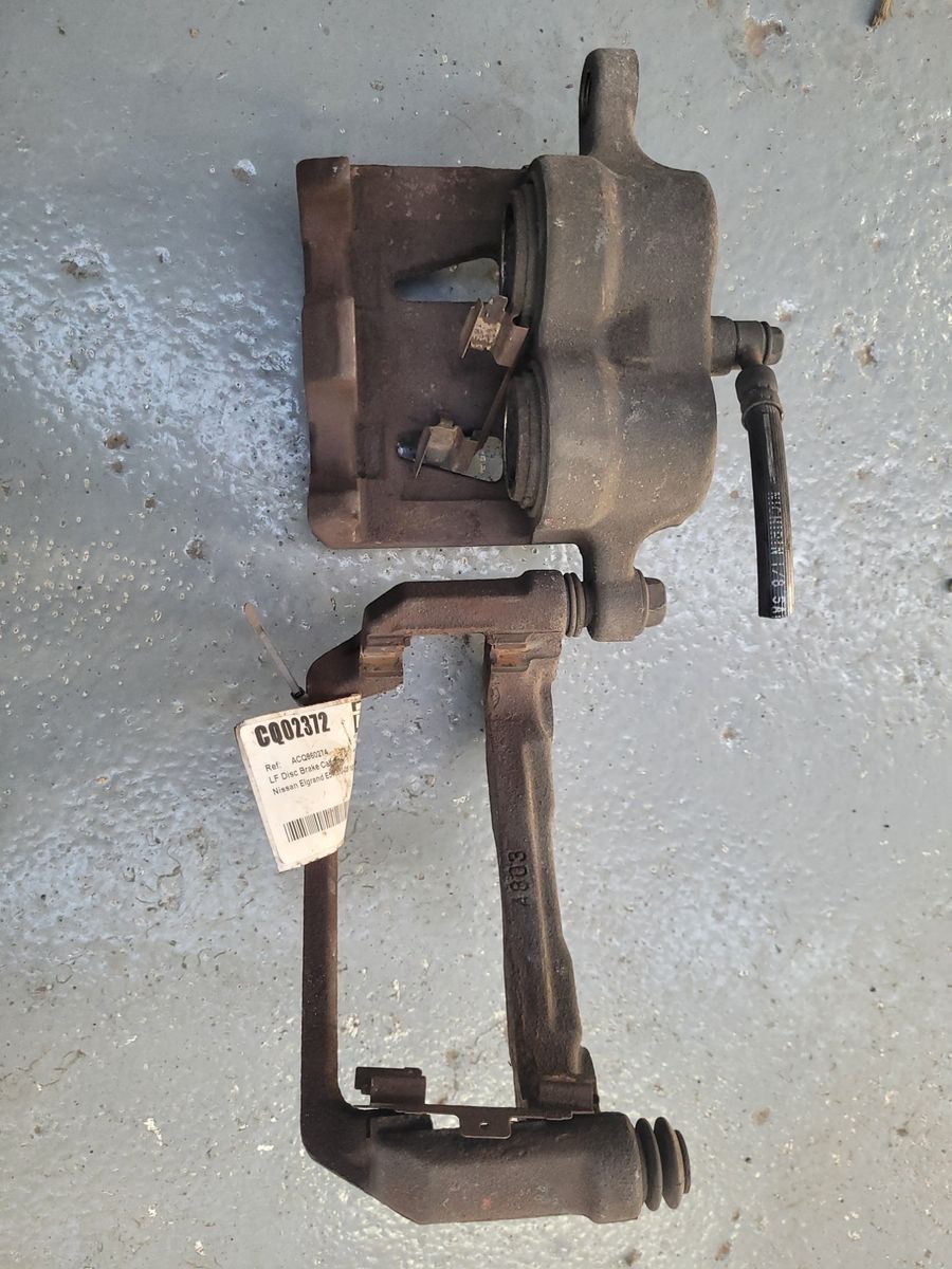 Dirty, used brake caliper and bracket assembly on concrete floor