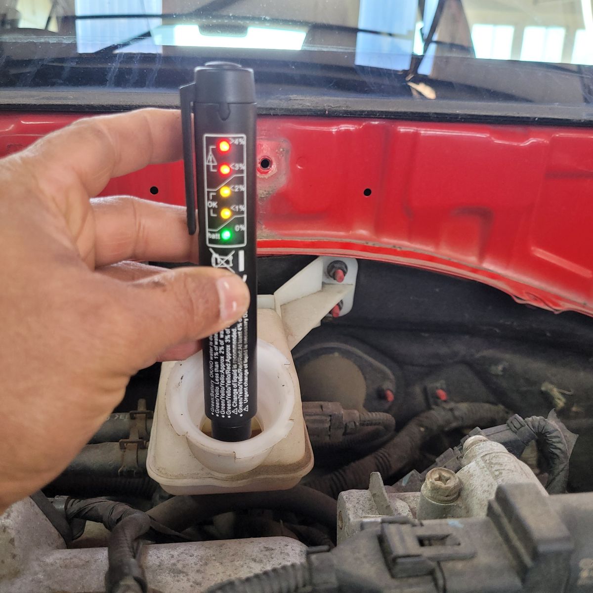 Hand using a brake fluid tester in a car's brake fluid reservoir