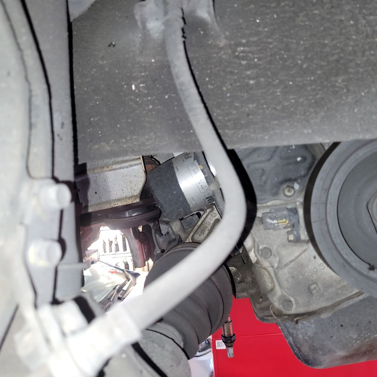 Close-Up View of Automotive Brake Hose and Engine Components Brake hose and engine parts visible beneath a car's undercarriage.