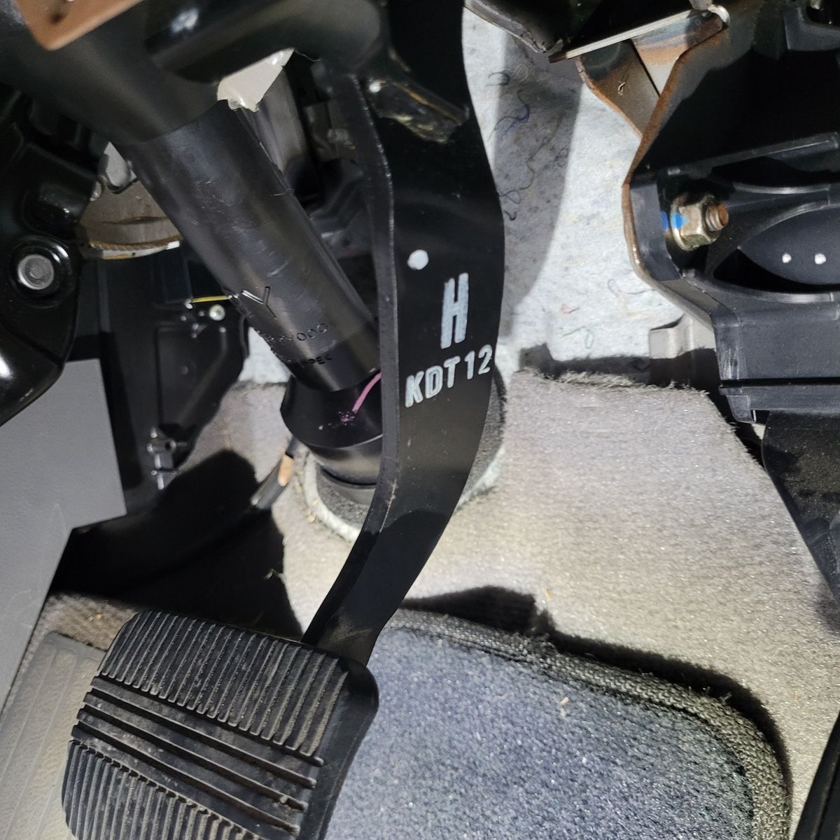 Black brake pedal over car floor mat and carpet under dashboard