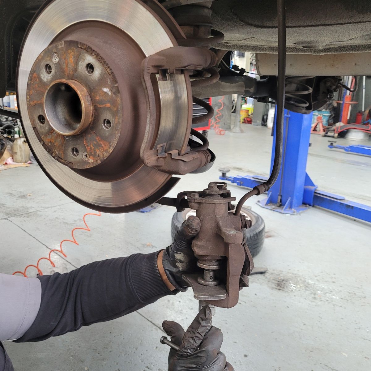Mechanic's gloved hands removing brake caliper and pads from car disc