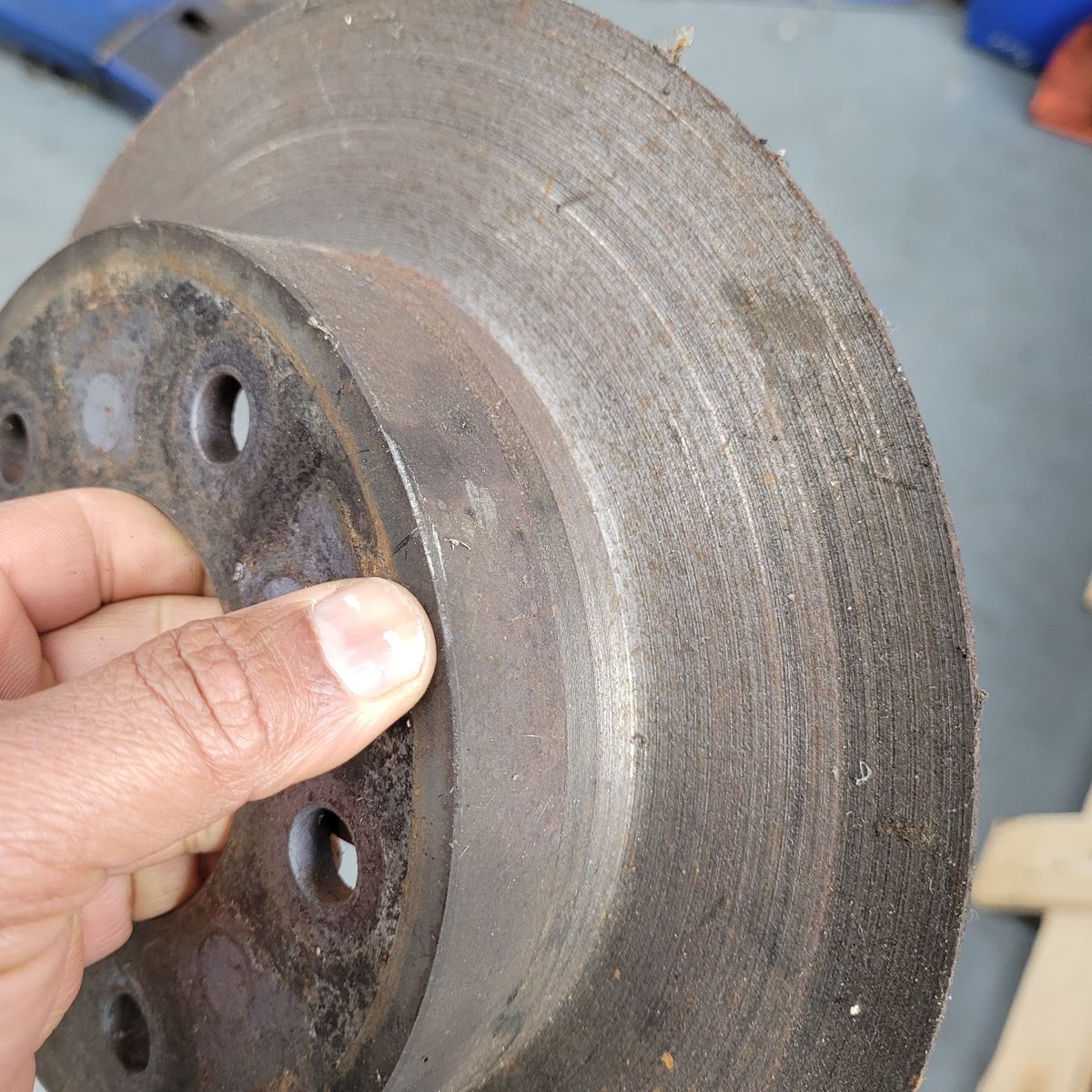 Worn Brake Rotor Close-Up Hand holding an old, grooved brake rotor with visible rust and wear.