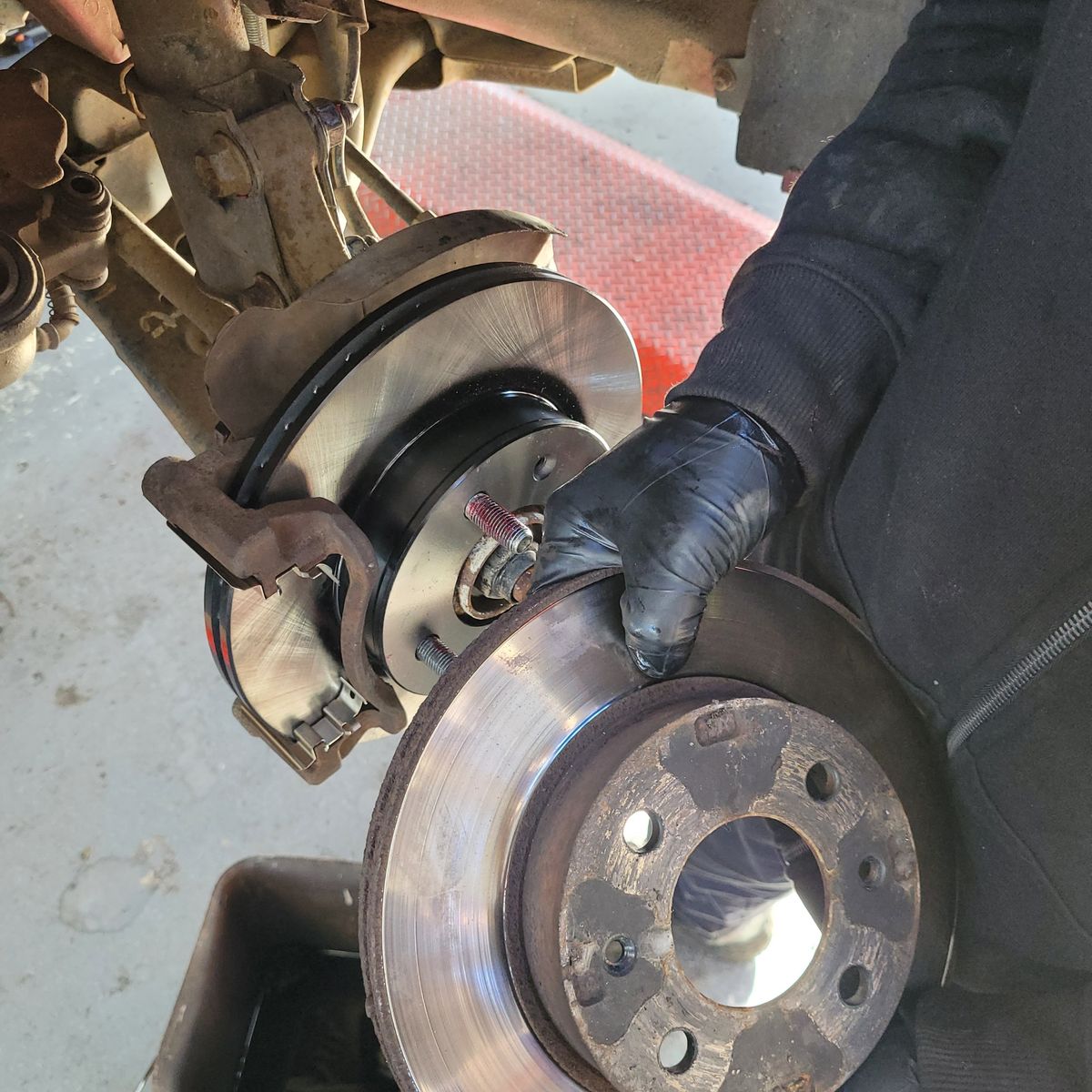 Gloved mechanic holding old brake rotor near newly installed rotor on vehicle