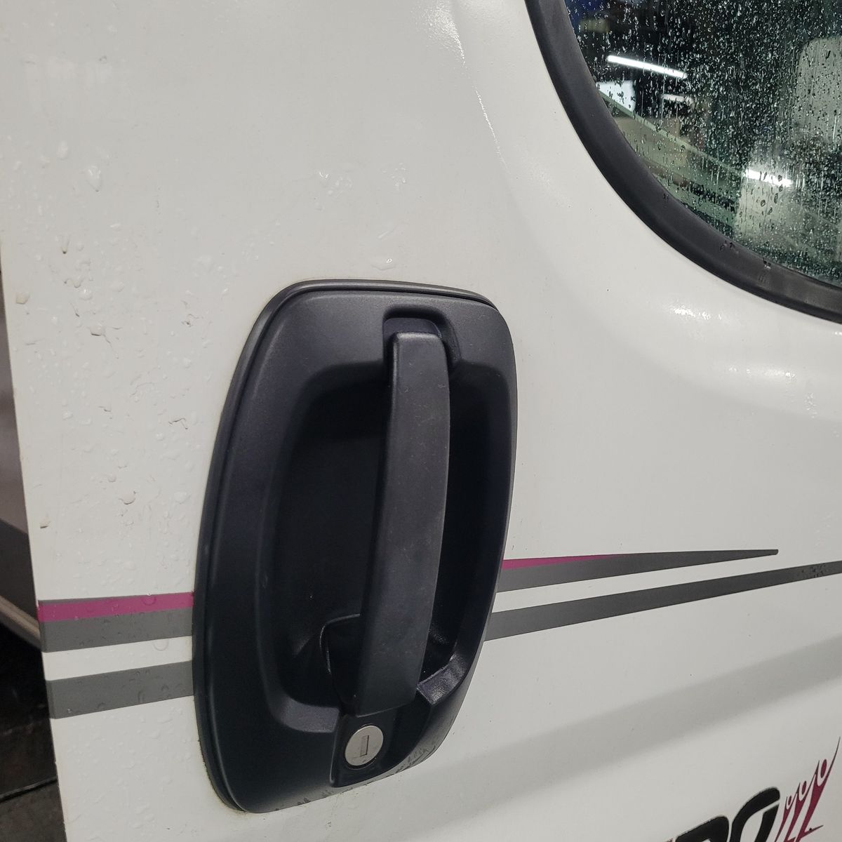 Close-up of Camper Van Door Handle Black door handle on a white camper van with raindrops and stripes.