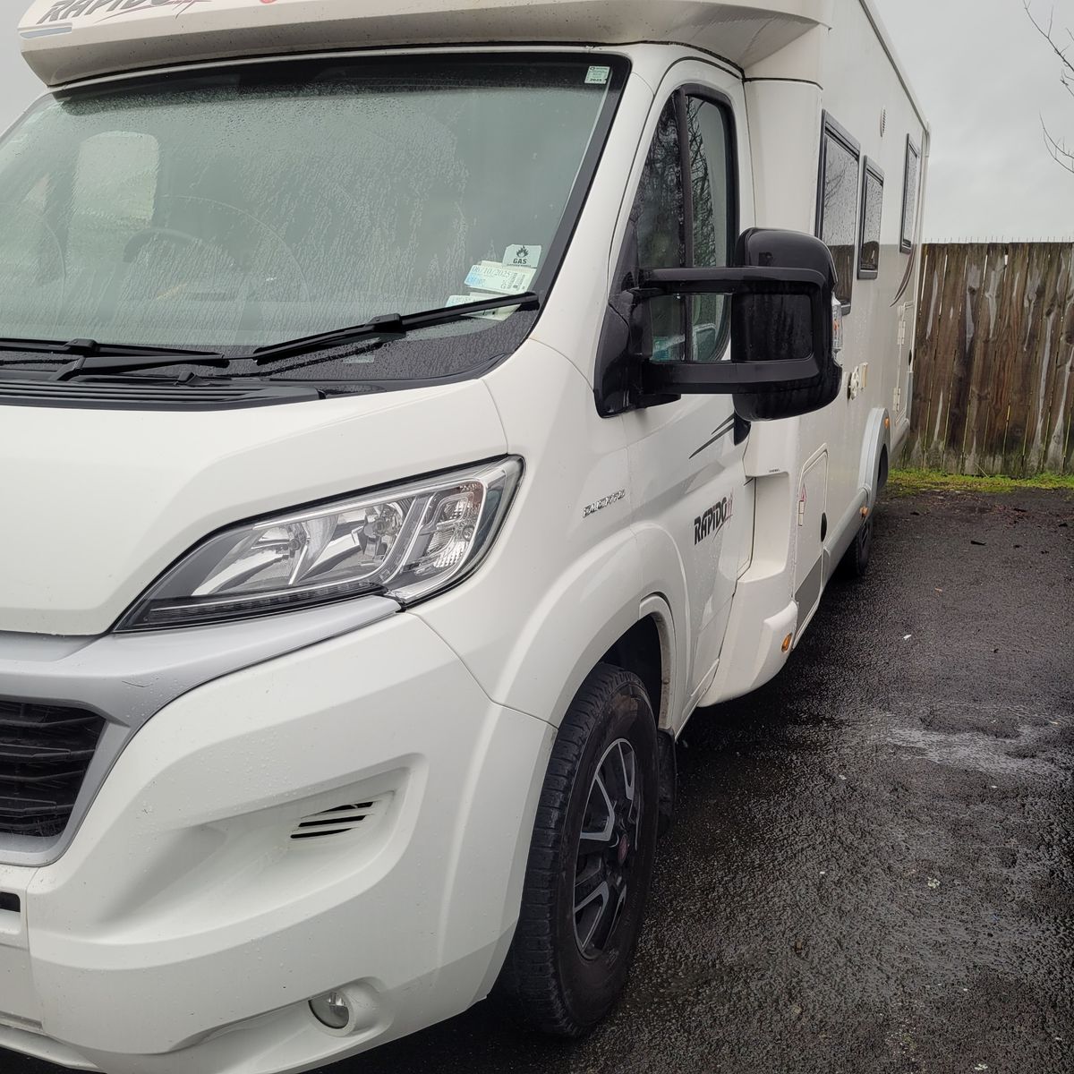 Modern White Camper Van Parked on Wet Asphalt Front side view of a white camper van parked on a rainy day