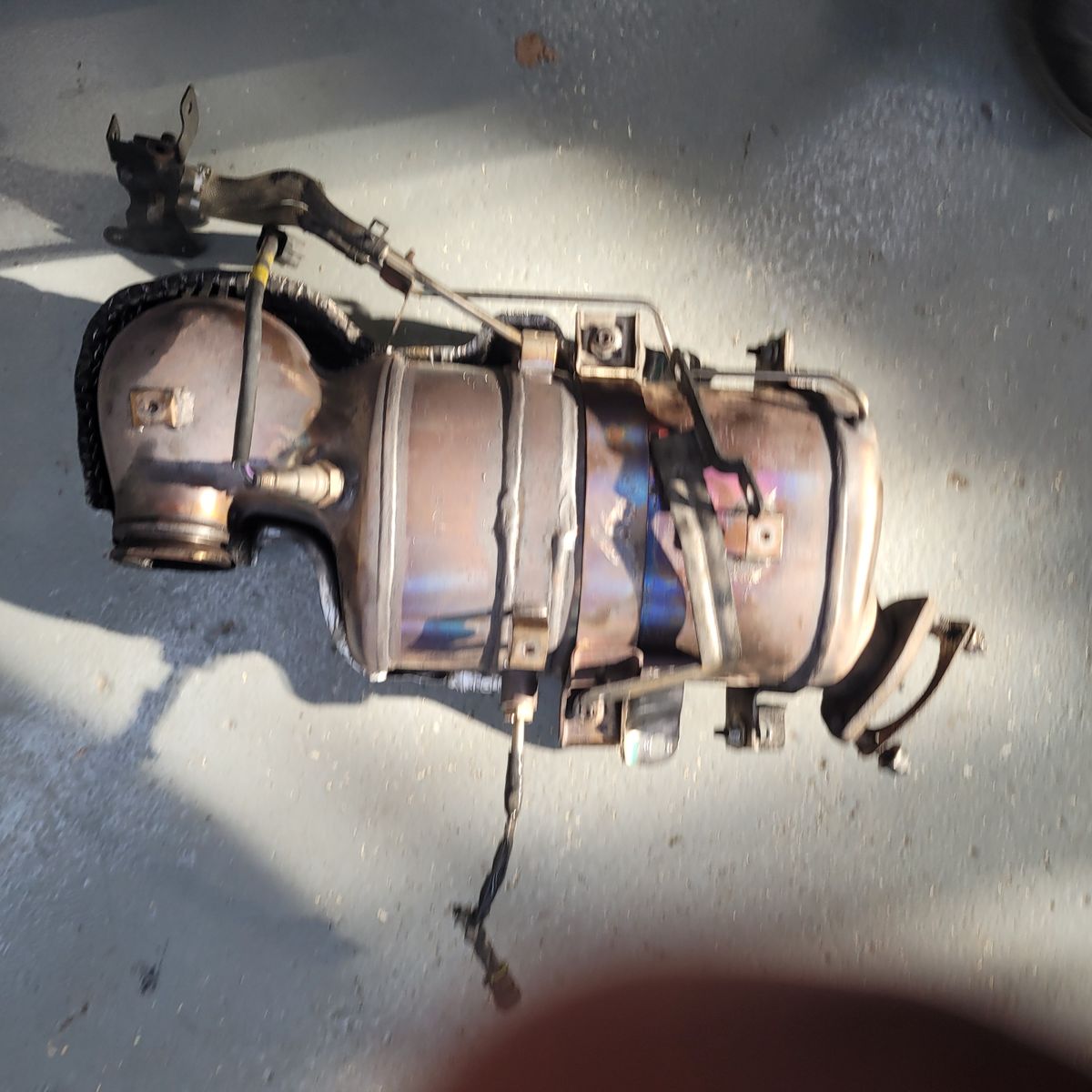 Used Catalytic Converter on Workshop Floor Rusty catalytic converter detached and resting on a gray floor