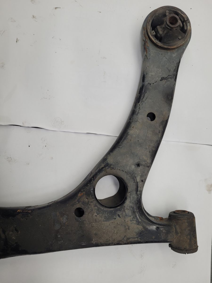 Used vehicle control arm with bushings, placed on a white surface