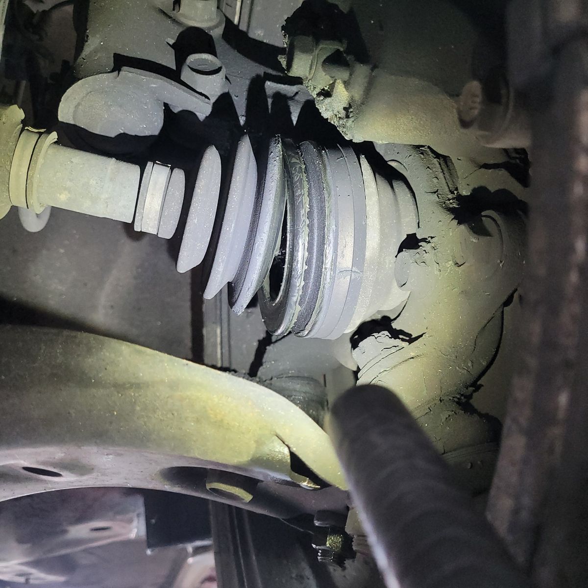 Close-up of torn CV boot with visible grease and axle parts.