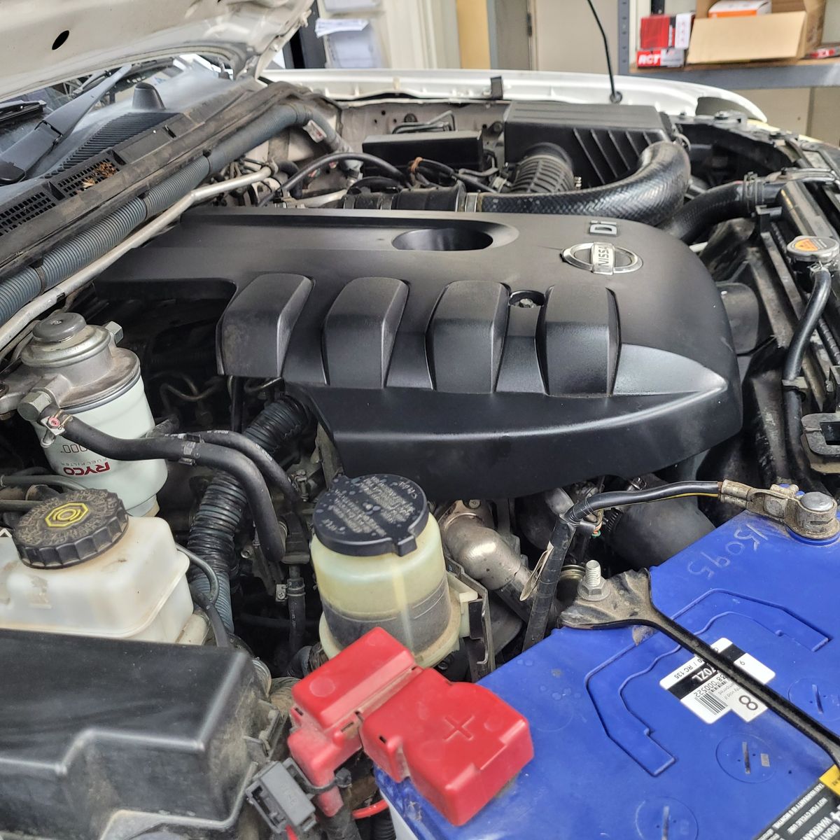 Close-Up of Modern Diesel Engine Compartment Diesel engine with visible Nissan cover, battery, and fluid reservoirs under the hood.