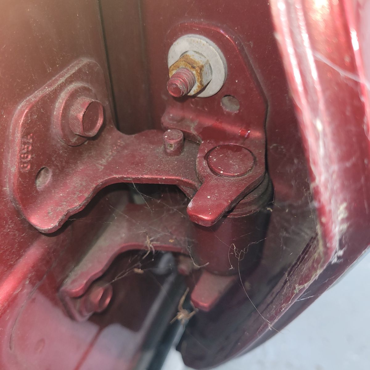 Close-Up of Car Door Hinge Mechanism Detailed view of a maroon car door hinge with bolts and cobwebs.