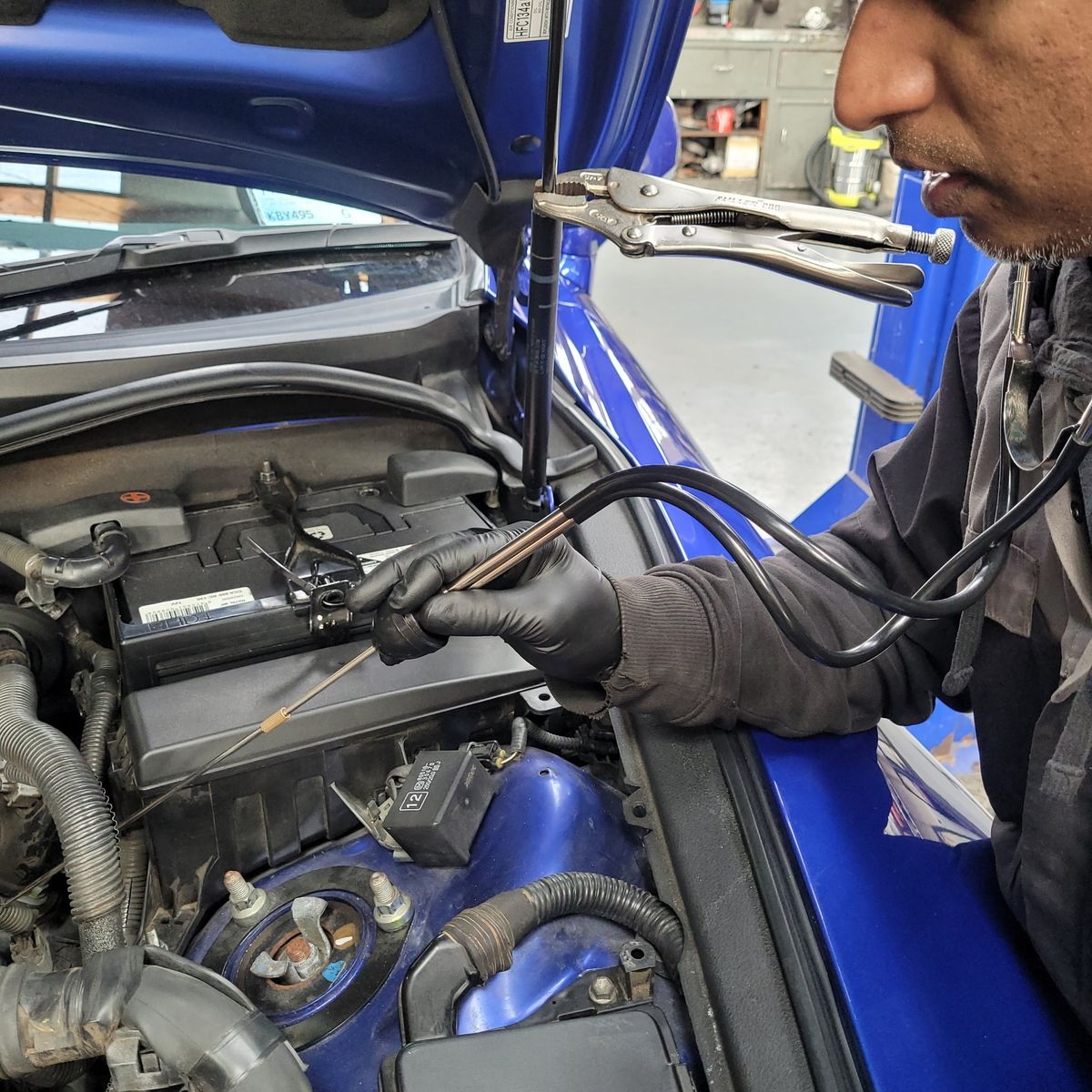 Mechanic using an automotive stethoscope to check engine noise in a car.