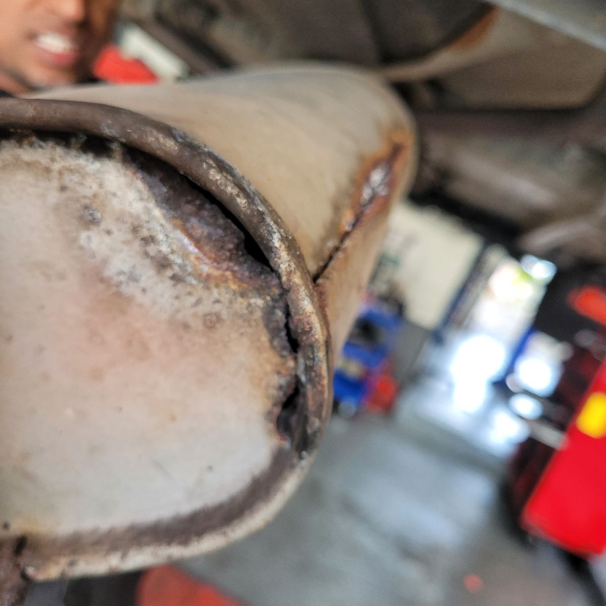 Exhaust Leak on Rusted Muffler Close-up of a cracked, rusted car muffler showing an exhaust leak.