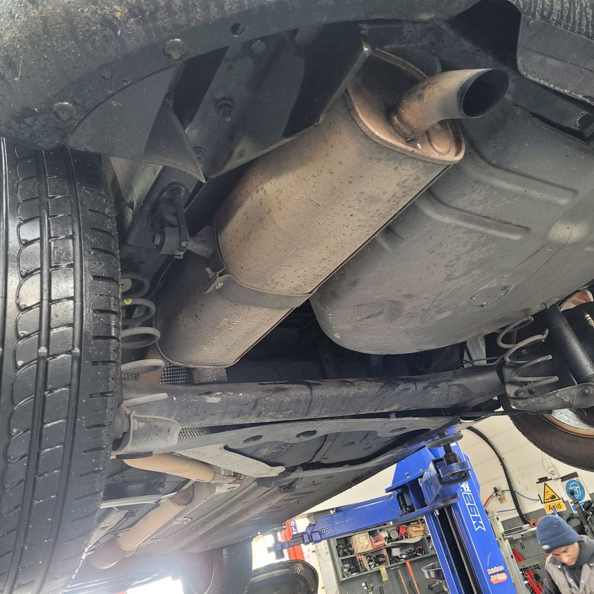 Exhaust system and muffler visible beneath a raised vehicle in a garage