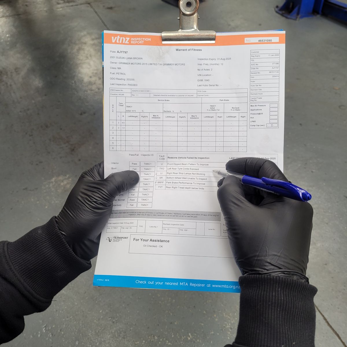Mechanic Reviewing VTNZ Warrant of Fitness Inspection Report Gloved hands holding and marking a VTNZ Warrant of Fitness inspection sheet.