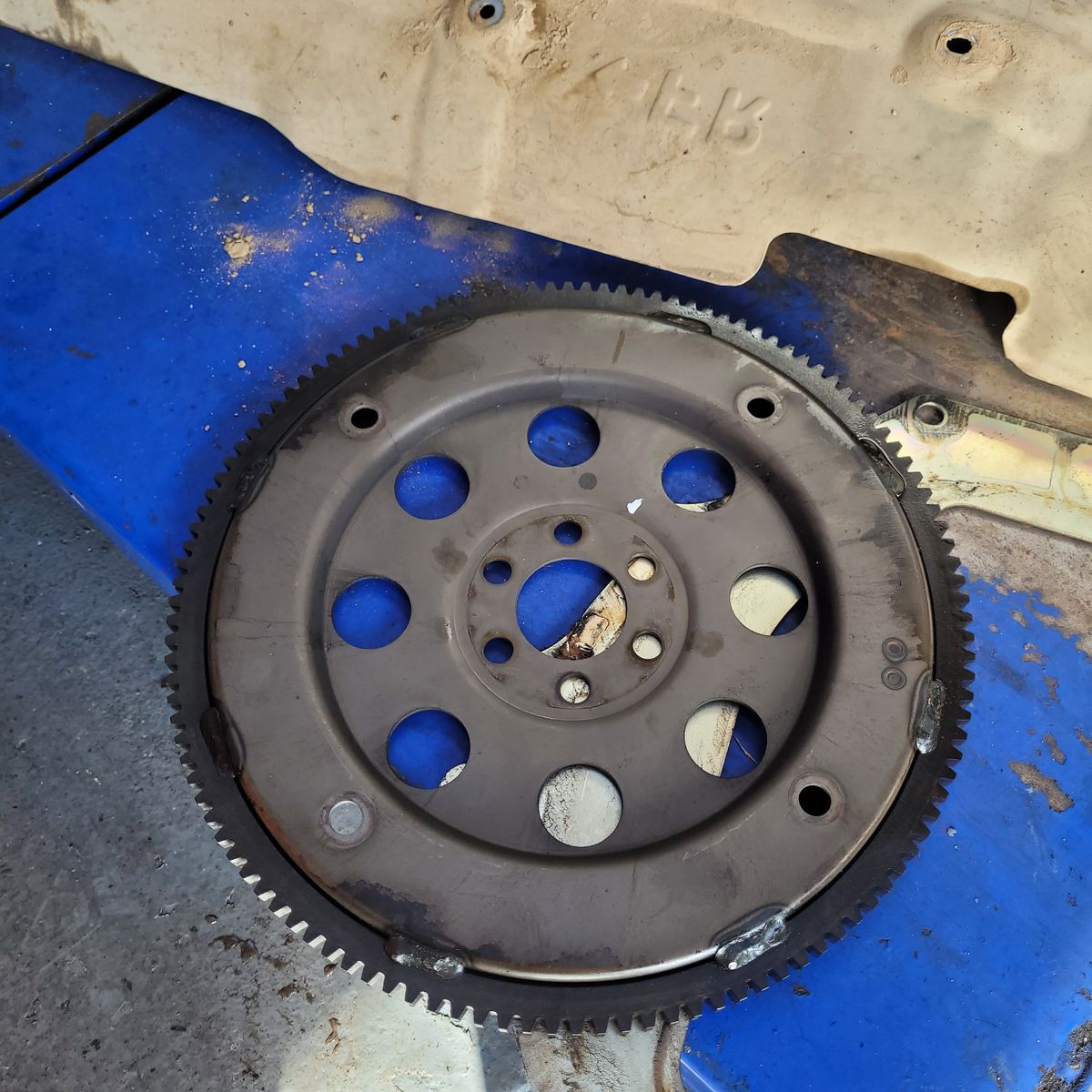 Automotive Flywheel on Workshop Floor Circular metal flywheel with gear teeth, resting on blue surface