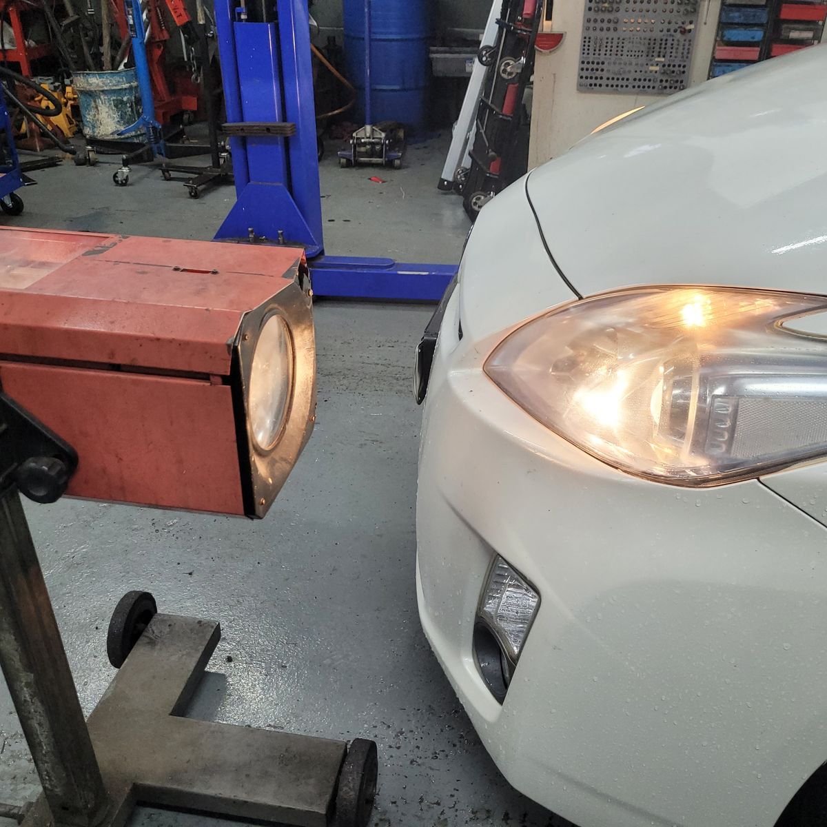 Close-up of car headlight being aligned with a beam alignment tester in a garage.