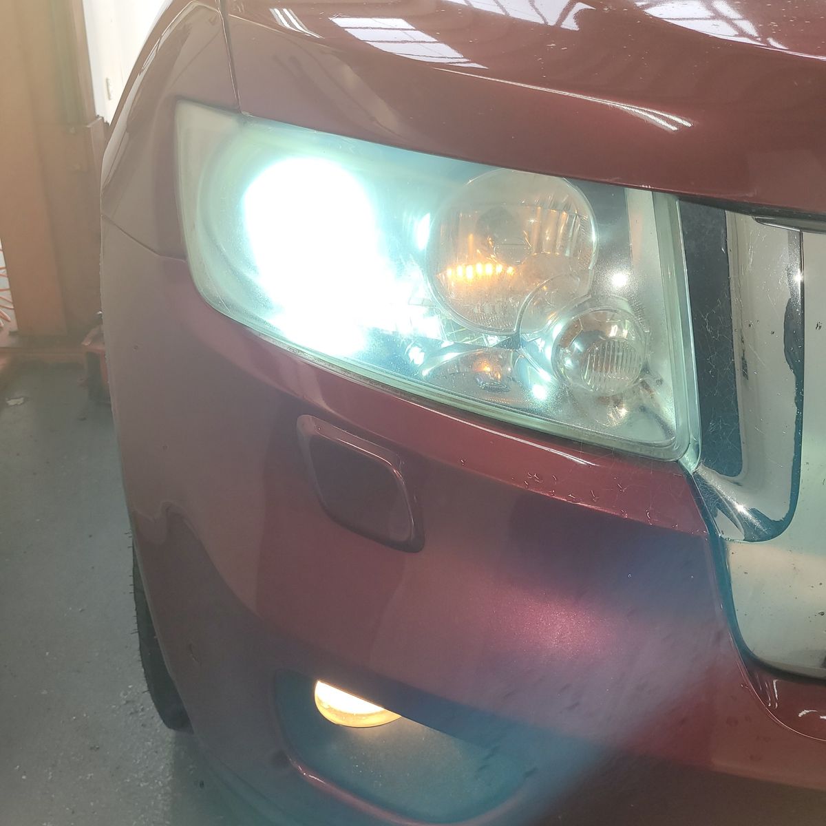 Car With Dim Headlight Close-up of a car's dim, foggy headlight on a maroon vehicle