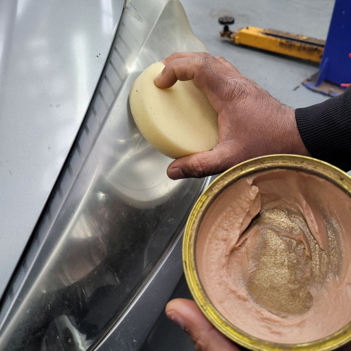 Hand using sponge and paste to clean foggy car headlight lens