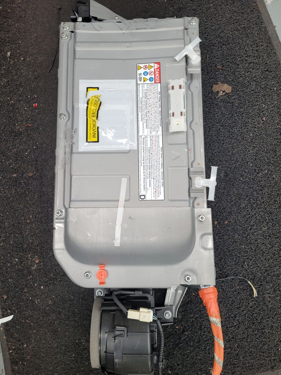 Rectangular hybrid car battery pack with warning labels and orange electrical cable