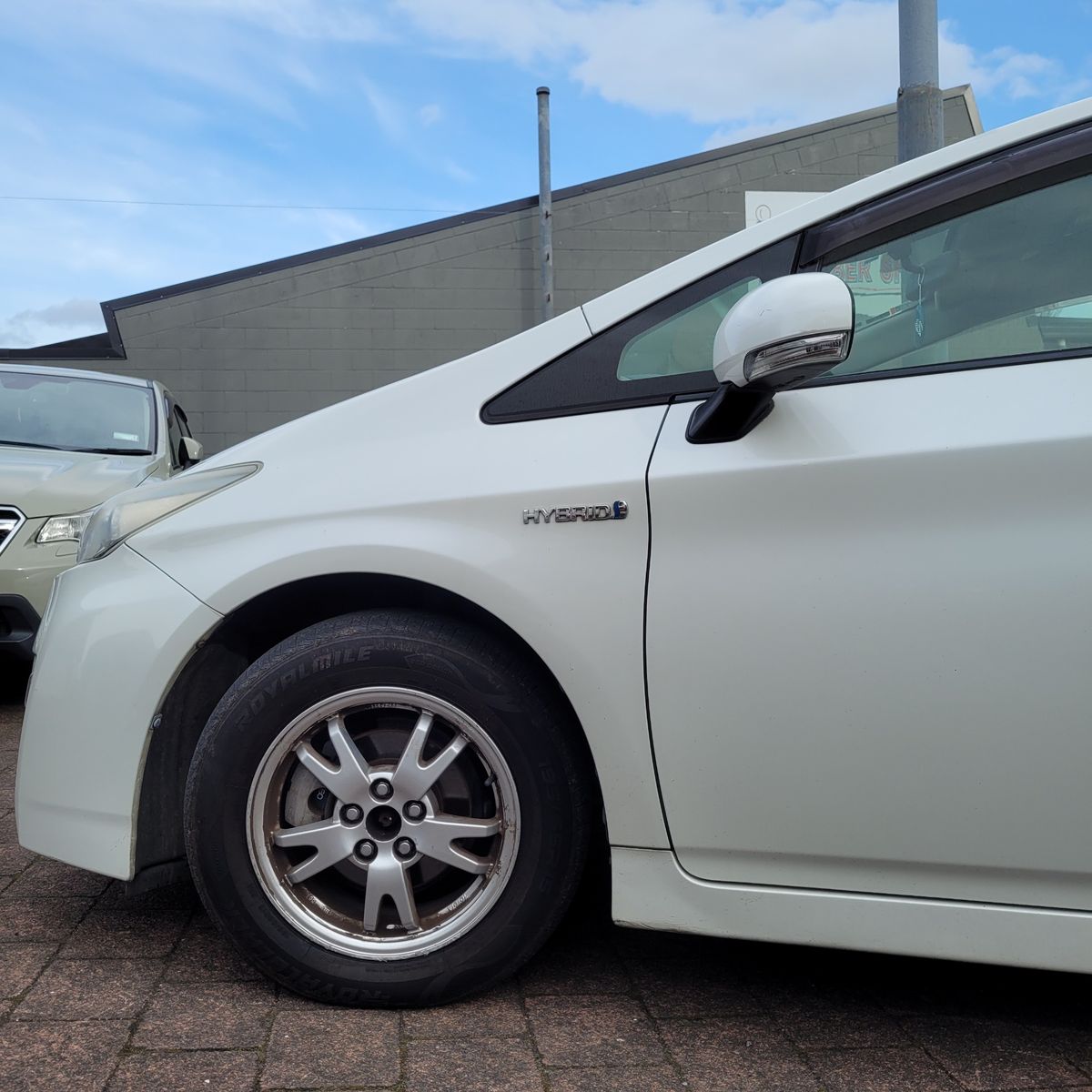 White Hybrid Car Parked on Brick Pavement Front side view of a white hybrid car with visible hybrid badge