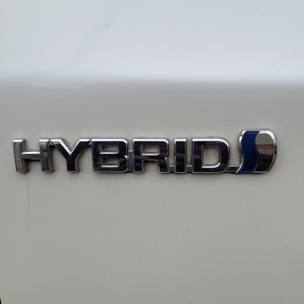 Shiny chrome hybrid badge on a white car