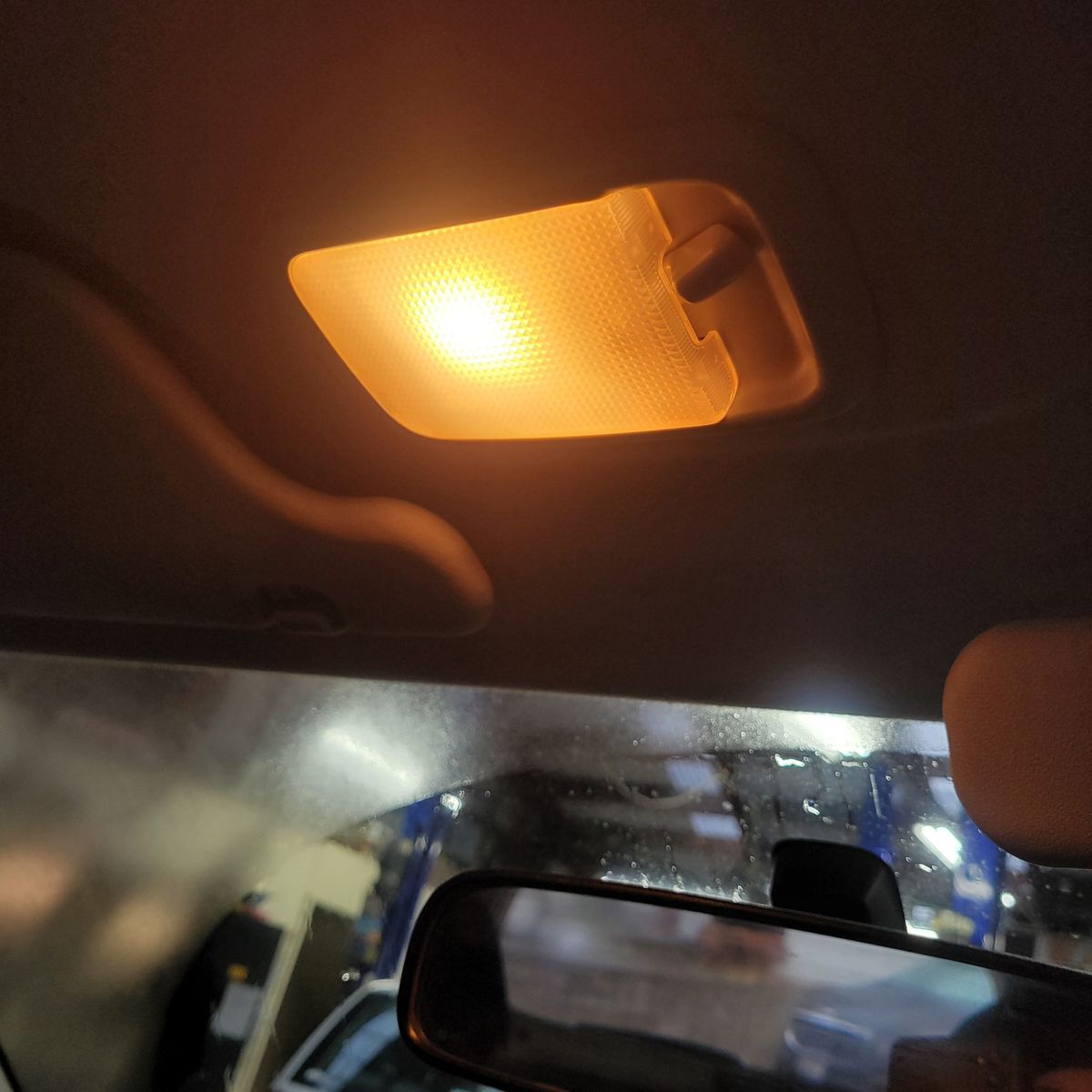 Warm yellow dome light glowing inside a car, above the rearview mirror.