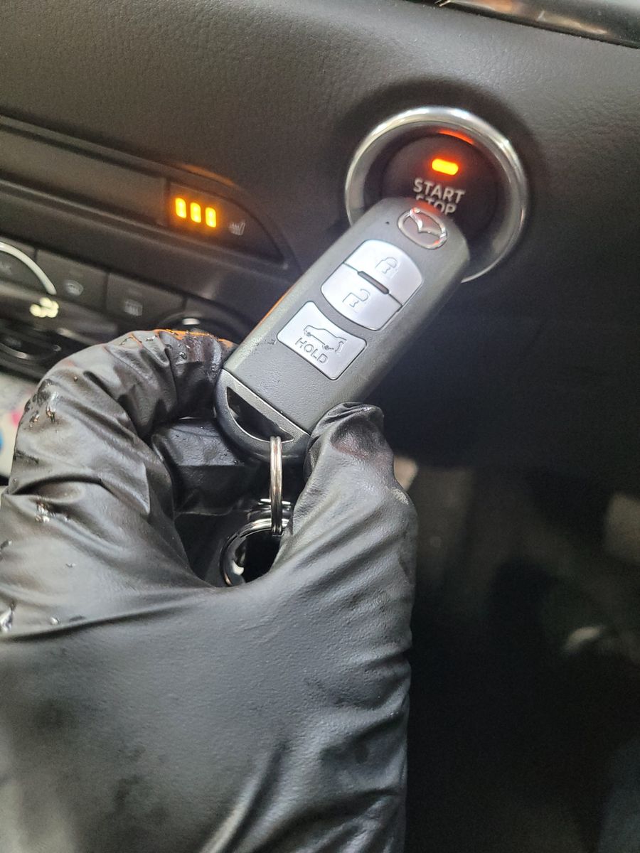 Gloved hand holding a Mazda key fob near a car's push start button
