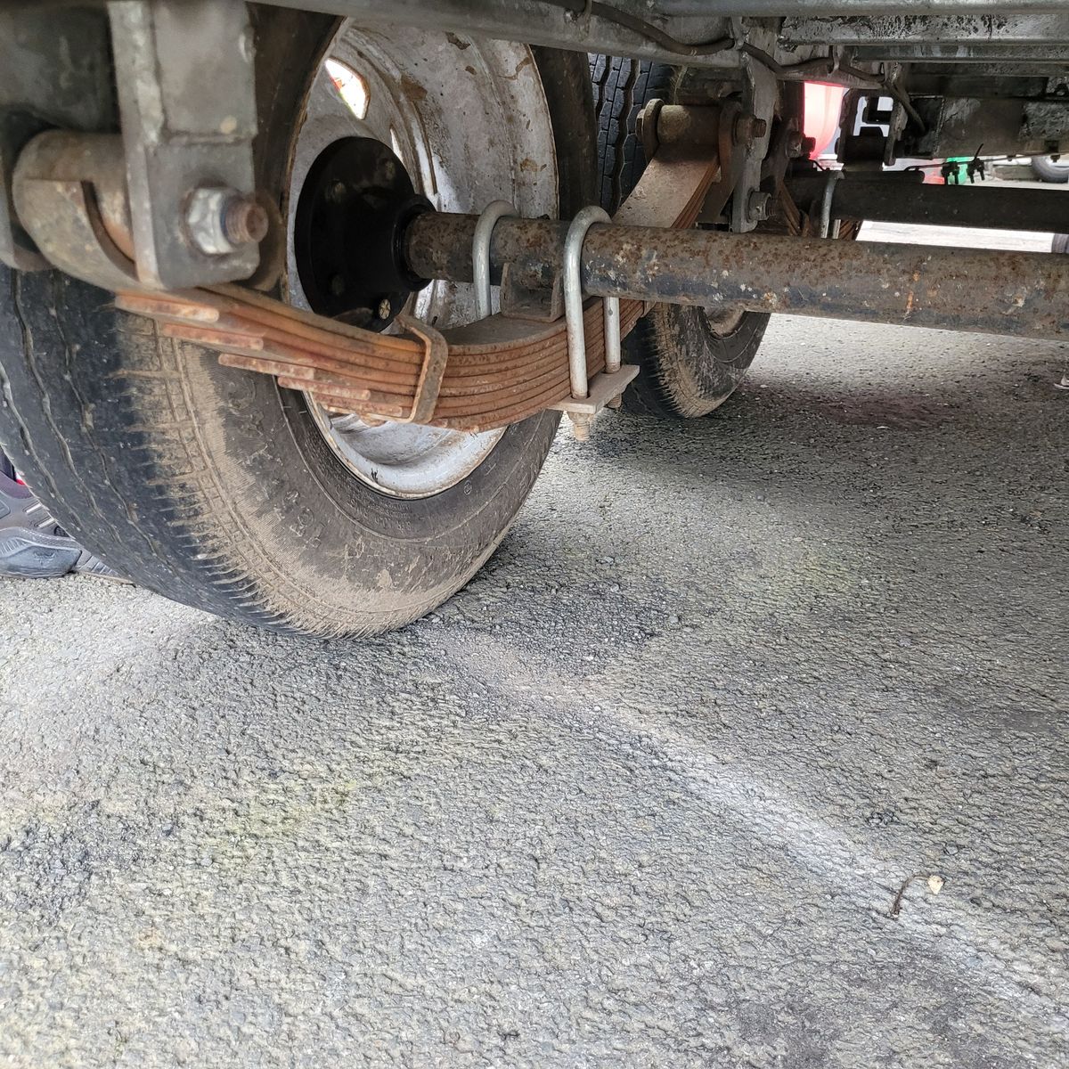 Close-up of a leaf spring suspension attached to a vehicle's axle beneath the wheel.