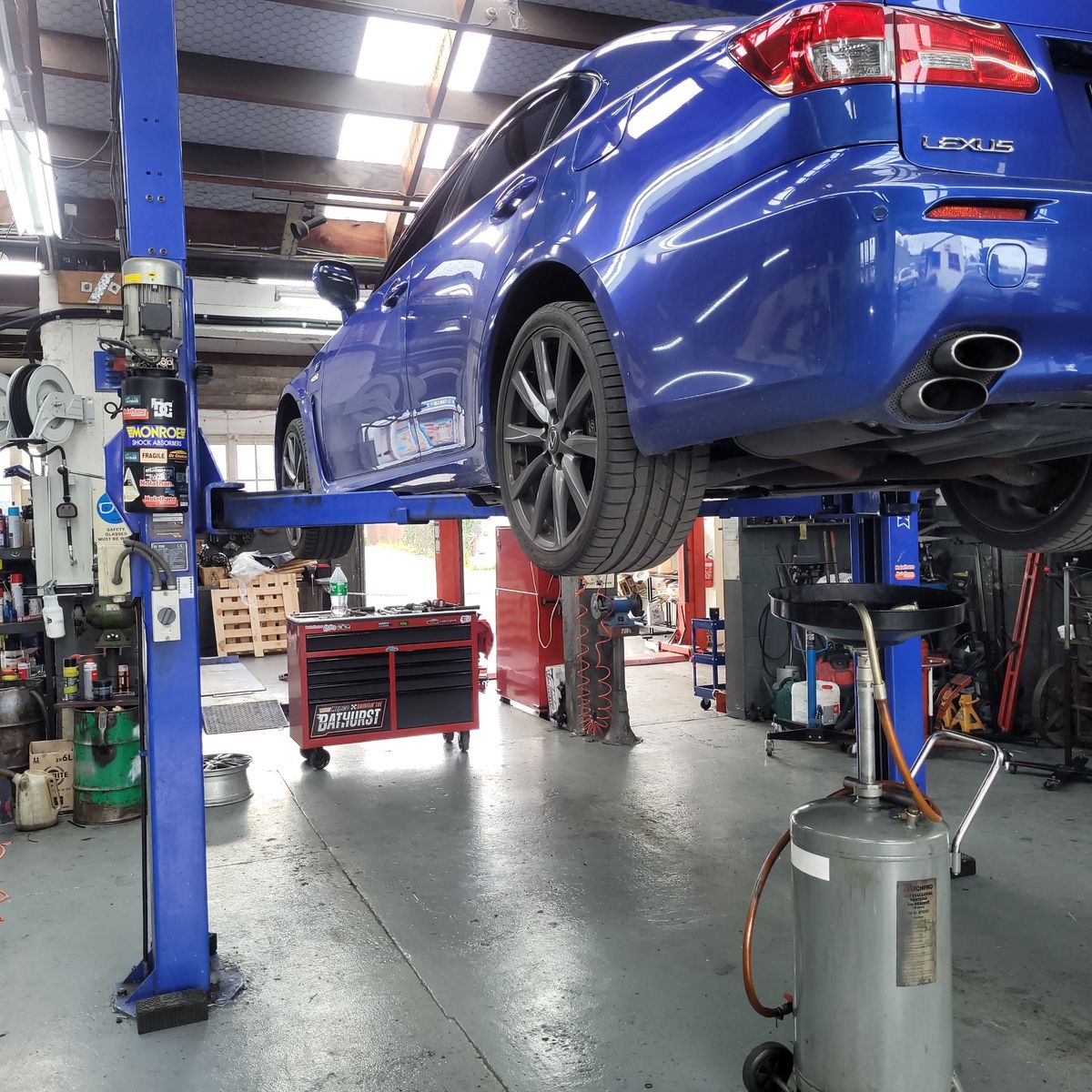 Blue Lexus sedan elevated on a hydraulic lift in an auto repair shop.