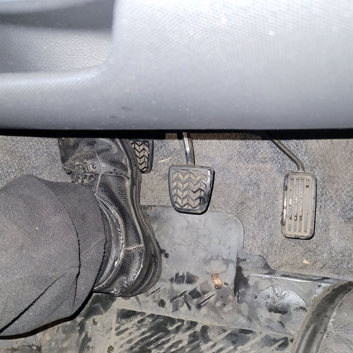 Person's foot pressing the clutch pedal of a manual transmission car