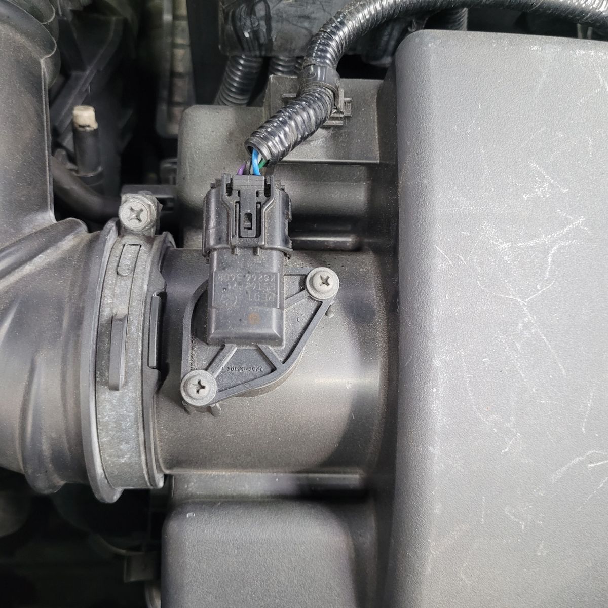 Close-up of a mass air flow sensor installed in a car's air intake system.