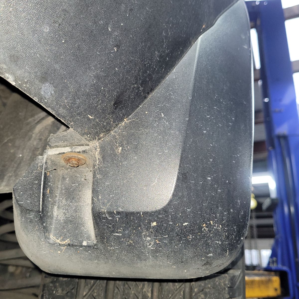 Dirty black mudflap secured with a rusty screw on a vehicle